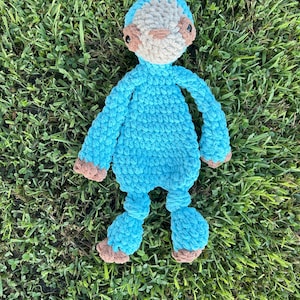 May include: A crocheted blue sloth toy with brown accents lying on green grass.