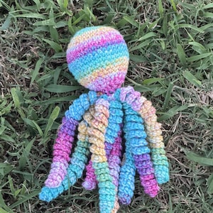 May include: A crocheted octopus toy featuring a round head and eight spiraled tentacles. The yarn is variegated with a blend of bright pink, light blue, yellow, and purple colors throughout the entire structure of the handmade stuffed animal.