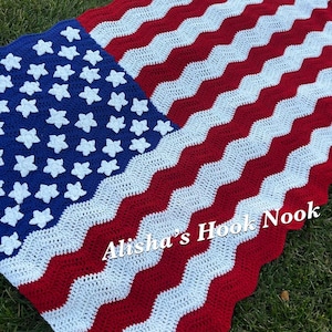May include: A crocheted blanket featuring a red, white, and blue chevron pattern with white stars appliqued on a blue field. The text Alisha's Hook Nook is printed in white across the lower section of the blanket, which mimics the American flag.