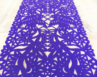May include: Purple table runner with a delicate, intricate cut-out design featuring flowers and leaves. The runner is made of a thick, felt-like material.