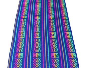 May include: A blue table runner with a colorful geometric pattern. The runner has a fringe border and is made of woven fabric.