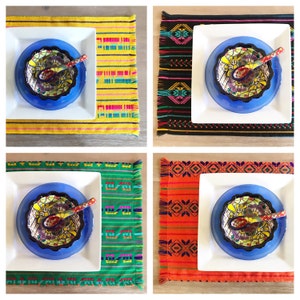 May include: Four placemats with different colorful patterns, each with a white plate, a blue bowl, and a small spoon. The placemats have fringe edges.