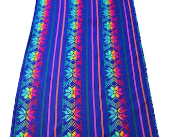 May include: A blue table runner with colorful stripes and floral patterns. The runner has a fringe on both ends.
