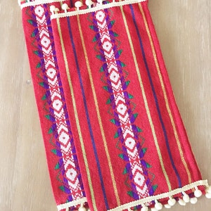May include: Two red and white striped fabric napkins with a white pom-pom trim. The napkins have a geometric pattern in green, purple, and white.