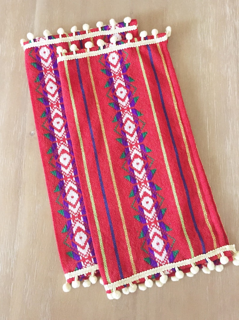 May include: Two red and white striped fabric napkins with a white pom-pom trim. The napkins have a geometric pattern in green, purple, and white.