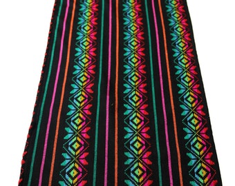 May include: A black table runner with colorful stripes and a geometric pattern. The runner has a fringe on the bottom edge.