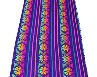 May include: A colorful table runner with a geometric pattern in shades of pink, green, orange, and yellow on a purple background. The runner has a fringe border.
