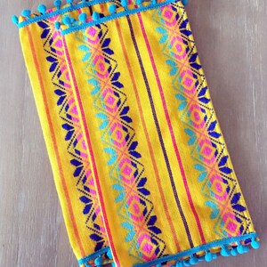 May include: Two yellow table runners with blue pom-pom trim and colorful geometric patterns.