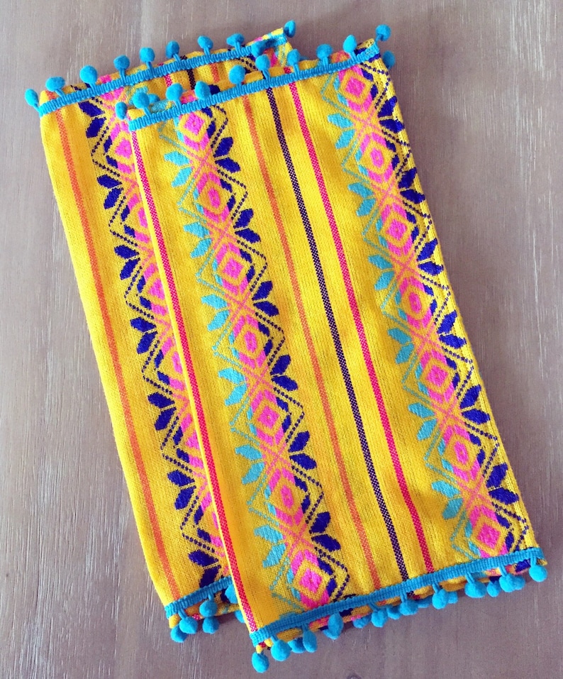May include: Two yellow table runners with blue pom-pom trim and colorful geometric patterns.