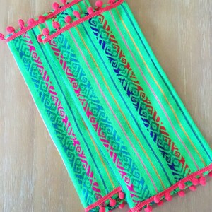 May include: Two green tea towels with a colorful geometric pattern and a pink pom-pom trim.