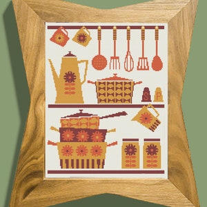 Op de afbeelding: Een ingelijst kruissteekontwerp met een keukenscène met verschillende potten, pannen en keukengerei in tinten oranje, bruin en rood. Het ontwerp bevat een koffiekan, een vergiet, een garde, een spatel en een set zout- en peperstrooiers.