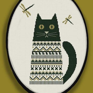 May include: A black cat wearing a green and gold patterned sweater with two green dragonflies on a white background.