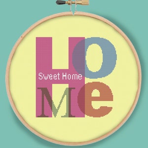 Puede incluir: Un aro de bordado amarillo con la palabra "Home" en letras coloridas que se superponen. Las letras están bordadas en rosa, azul, verde y naranja. El texto "Sweet Home" está bordado en blanco debajo de la palabra "Home".