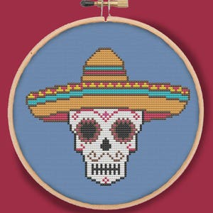 Può includere: Un teschio di zucchero colorato che indossa un tradizionale sombrero messicano. Il teschio è bianco con contorni neri e occhi rosa e neri. Il sombrero è marrone con rifiniture gialle, blu e rosse.
