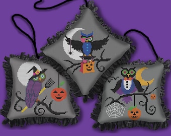 May include: Three gray fabric pillow ornaments with black fringe trim and black ribbon hangers. Each pillow features a different embroidered design of an owl with Halloween-themed details, including a witch's hat, a jack-o-lantern, and a crescent moon.