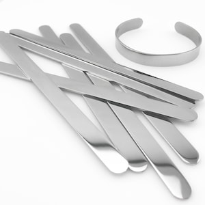 May include: A set of silver metal strips, some are straight and some are bent into a curved shape. The strips are arranged in a criss-cross pattern. A silver metal bracelet is also included in the image.