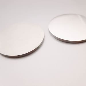 May include: Two round, silver-colored coasters on a white surface.