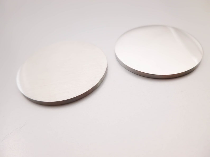 May include: Two round, silver-colored coasters on a white surface.