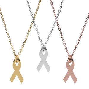 May include: Three necklaces with ribbon pendants. One is gold-colored, one is silver-colored, and the third is rose gold-colored. Each necklace has a delicate chain and a ribbon-shaped pendant, symbolizing awareness or support.