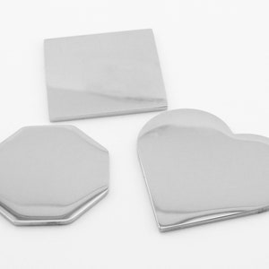 May include: Three blank metal tags in different shapes: a square, an octagon, and a heart. The tags are silver and have a shiny finish.