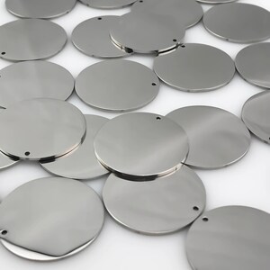 May include: A pile of silver metal circles with a small hole in the center of each circle.