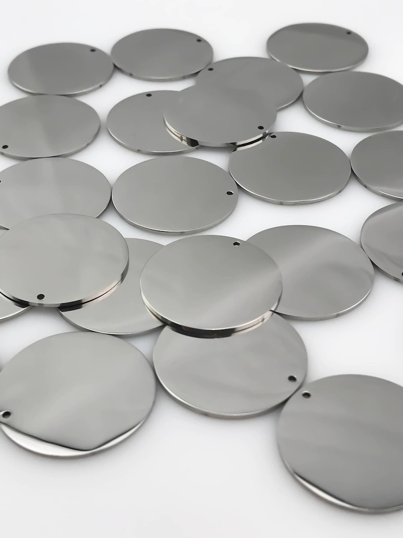 May include: A pile of silver metal circles with a small hole in the center of each circle.