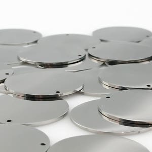 Pu&ograve; includere: Un mucchio di dischi rotondi in metallo argentato con un piccolo foro al centro. Questi dischi sono perfetti per creare gioielli, portachiavi o altri progetti fai-da-te.