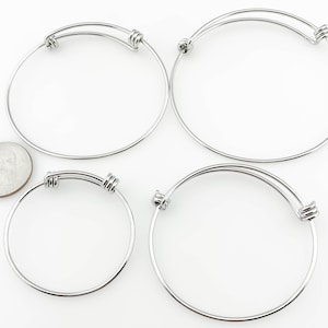 May include: Four silver expandable bangle bracelets. The bracelets are made of metal and have a simple, elegant design.
