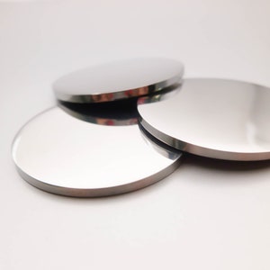 May include: Three round, silver-colored metal coasters. The coasters are stacked on top of each other.