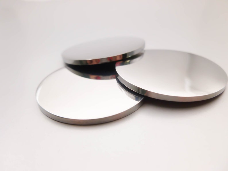 May include: Three round, silver-colored metal coasters. The coasters are stacked on top of each other.