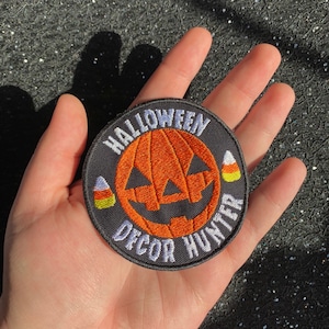Peut inclure: Un patch brodé noir et blanc avec une citrouille orange et le texte "Halloween Decor Hunter" et deux motifs de maïs sucré.