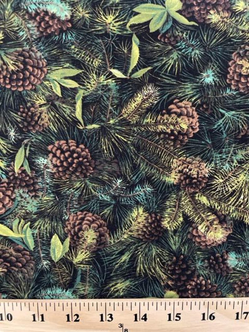 May include: A fabric print featuring brown pinecones and green pine needles on a black background. A wooden ruler is visible at the bottom, showing measurements from 10 to 17 cm, indicating the scale of the repeating botanical pattern.