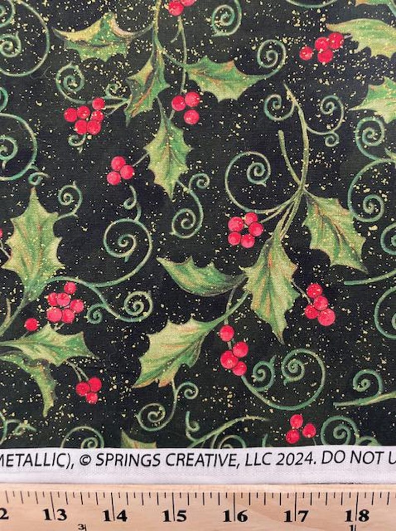 May include: A black fabric featuring a pattern of green holly leaves, red berries, and gold metallic swirls. The white selvage edge displays the text METALLIC, &copy; SPRINGS CREATIVE, LLC 2024. DO NOT U, positioned above a ruler showing inches.