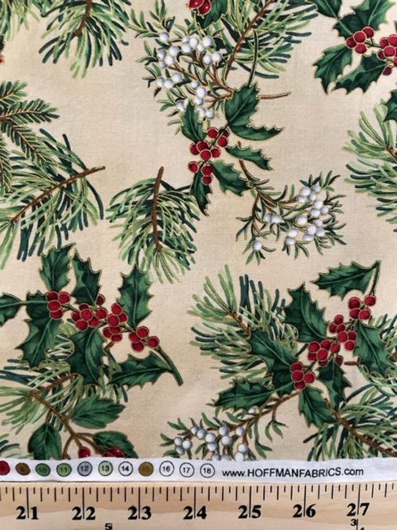 May include: A beige fabric featuring a repeating pattern of green pine needles, dark green holly leaves, clusters of red berries, and white berries. A white selvage edge displays colour circles, numbers 10 through 18, and HOFFMANFABRICS.COM.