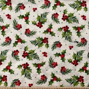 May include: A white fabric featuring a repeating pattern of green holly leaves and clusters of red berries, accented by small grey dots. A wooden ruler is visible at the bottom edge, showing measurements in centimetres for scale.