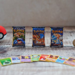 May include: Three miniature Pokemon trading card booster packs featuring Venusaur, Charizard, and Blastoise illustrations, accompanied by a red and white spherical toy, a circular metal coin, and eight individual trading cards arranged in a row.