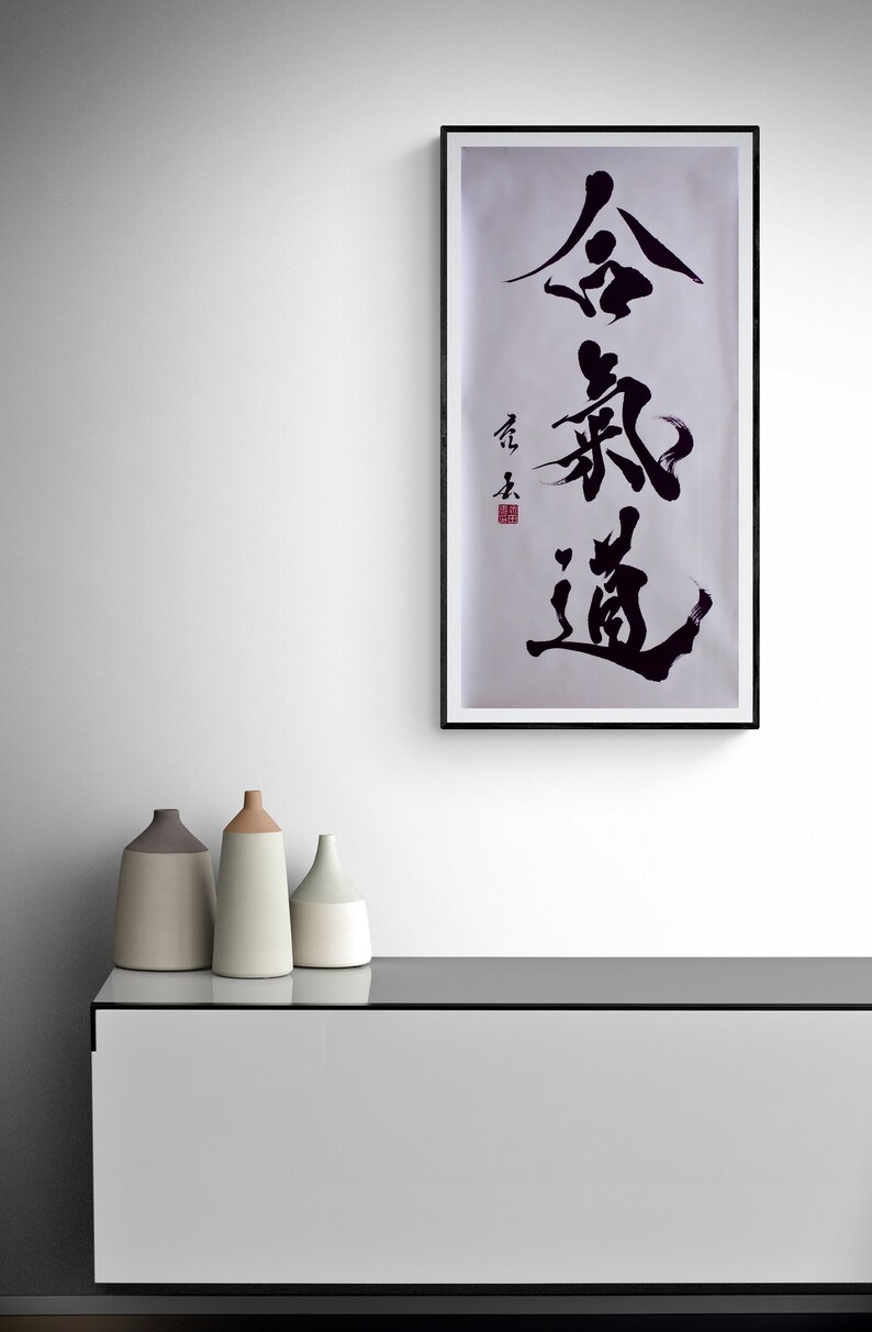 Puede incluir: Una impresi&oacute;n enmarcada en negro con fondo blanco y caligraf&iacute;a negra en caracteres chinos. La impresi&oacute;n est&aacute; colgada en una pared blanca sobre un armario blanco con tres jarrones de cer&aacute;mica en la parte superior.