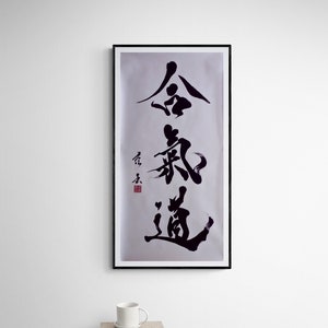 Puede incluir: Arte de caligraf&iacute;a en blanco y negro en un marco negro sobre una pared blanca. La caligraf&iacute;a dice "金 鍼 道", que se traduce como "El camino de la aguja de oro".