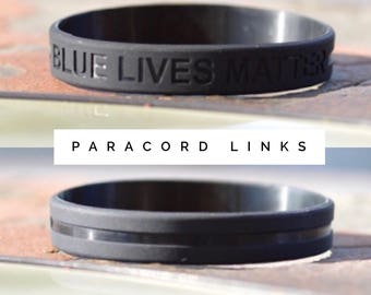 May include: Two black paracord bracelets. The top bracelet has the text "BLUE LIVES MATTER" embossed on it. The bottom bracelet has a single black stripe.