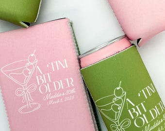 May include: Four green and pink can coolers with a martini glass design and the text "A TINI BIT OLDER" with a date. The text is in white.