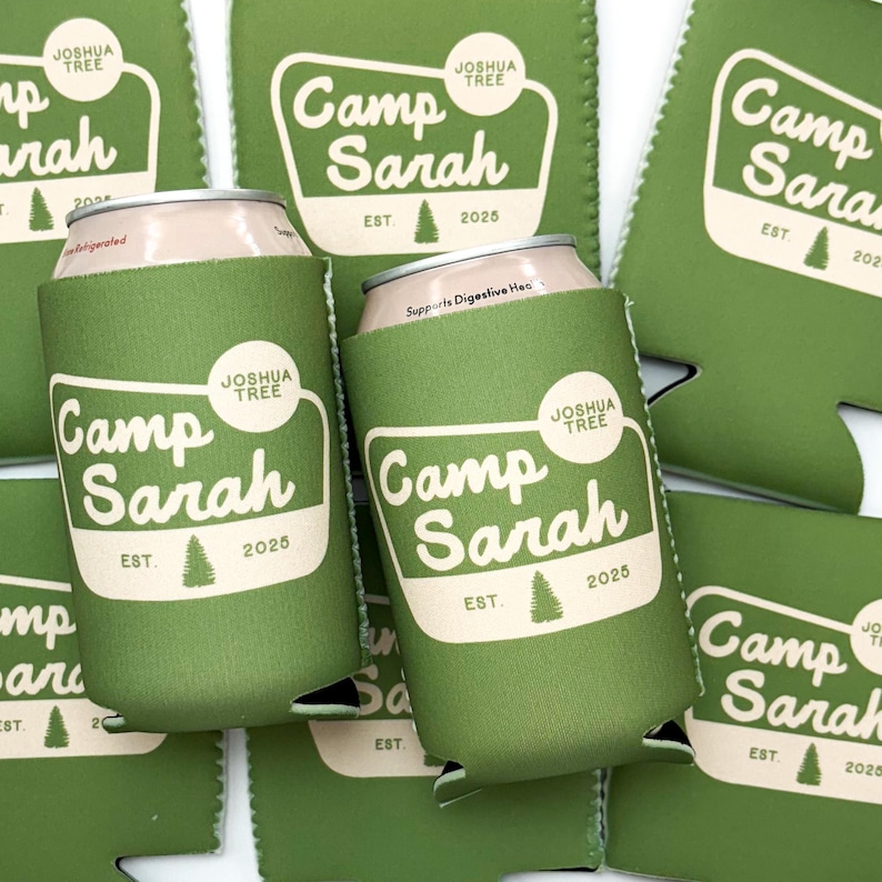 K&ouml;nnte beinhalten: Gr&uuml;ne und wei&szlig;e Getr&auml;nkedosenk&uuml;hler mit dem Aufdruck "Camp Sarah" und "Est. 2025". Die K&uuml;hler werden von Joshua Tree hergestellt.