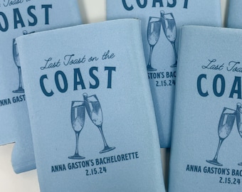 May include: Light blue can coolers with the text "Last Toast on the Coast" and a graphic of two champagne glasses clinking. The text "Anna Gaston's Bachelorette 2.15.24" is printed on the bottom of the cooler.
