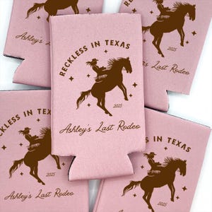 May include: Pink can cooler with a brown silhouette of a cowgirl riding a horse. The text "Reckless in Texas" and "Ashley's Last Rodeo" are printed on the cooler. The year 2025 is also printed on the cooler.