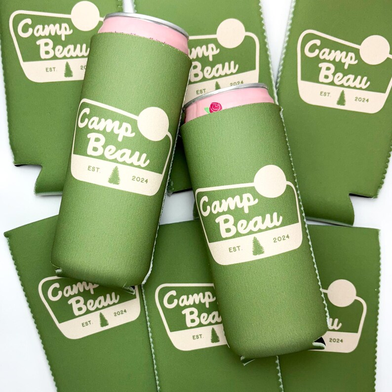 K&ouml;nnte beinhalten: Sechs gr&uuml;ne Neopren-Getr&auml;nkedosenk&uuml;hler mit dem Aufdruck "Camp Beau" und "EST 2024". Die K&uuml;hler sind &uuml;bereinander gestapelt.