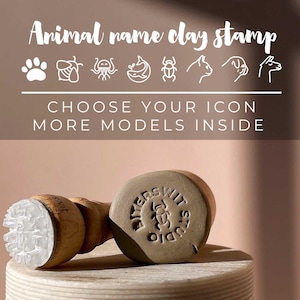 Può includere: Un timbro di argilla in legno con una testa del timbro circolare e un manico. La testa del timbro ha un design dettagliato e il testo "Animal name clay stamp" è in alto. Il timbro è su una superficie beige.