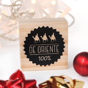 May include: A wooden stamp with a black and white design. The design features three camels with riders and the text "DE ORIENTE 100%".
