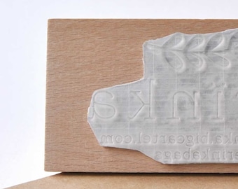 May include: A wooden block stamp with the text "ink &" and the website address "agedx.ink.bigcartel.com".