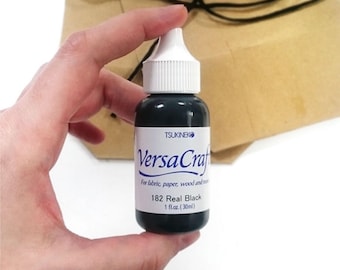 Puede incluir: Una pequeña botella de tinta negra etiquetada "VersaCraft" para tela, papel, madera y más. La botella está etiquetada "182 Real Black" y contiene 1 fl. oz. (30 ml) de tinta.