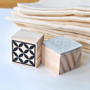 May include: Two wooden stamps with different designs. The first stamp has a black and white geometric pattern. The second stamp has a clear rubber surface with a pattern of circles.