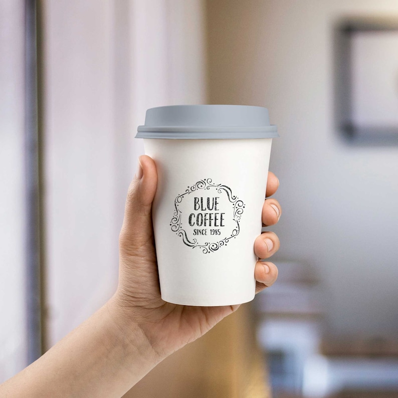 May include: A white to-go coffee cup with a gray lid. The cup has a black logo that says "Blue Coffee" with a decorative border and the text "Since 1985".